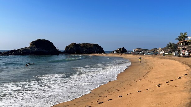 A beach with clear skies, rocky outcrops, and a sandy shore.