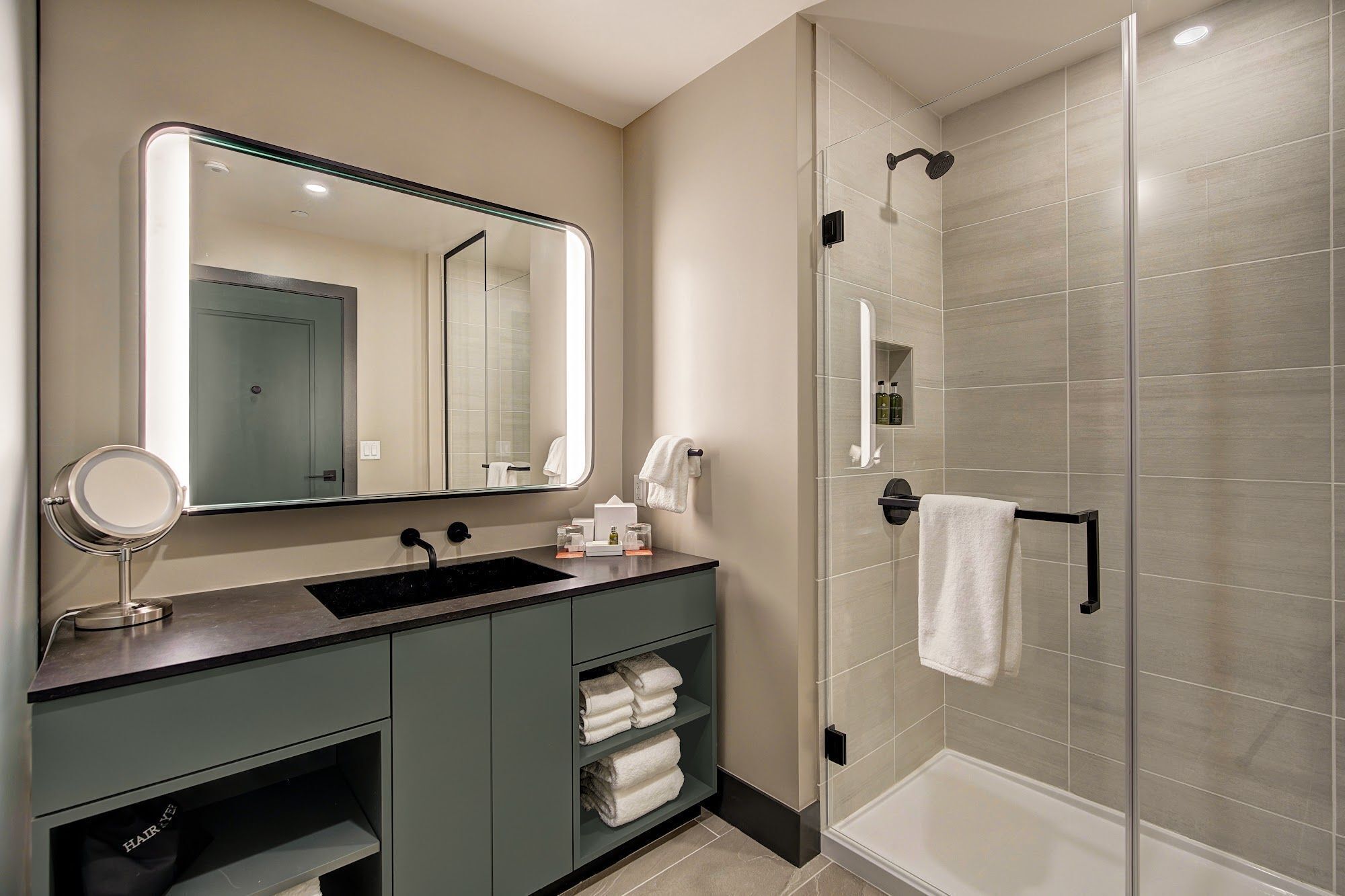 A modern bathroom with a large mirror, a sink, a vanity, and a glass-enclosed shower area.