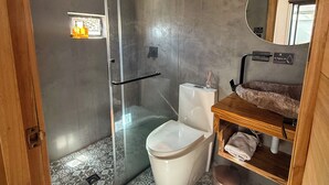A modern bathroom with a glass-enclosed shower, a white toilet, a wooden vanity with a mirror, and patterned floor tiles. - Hotel Dubai (Cuenca)