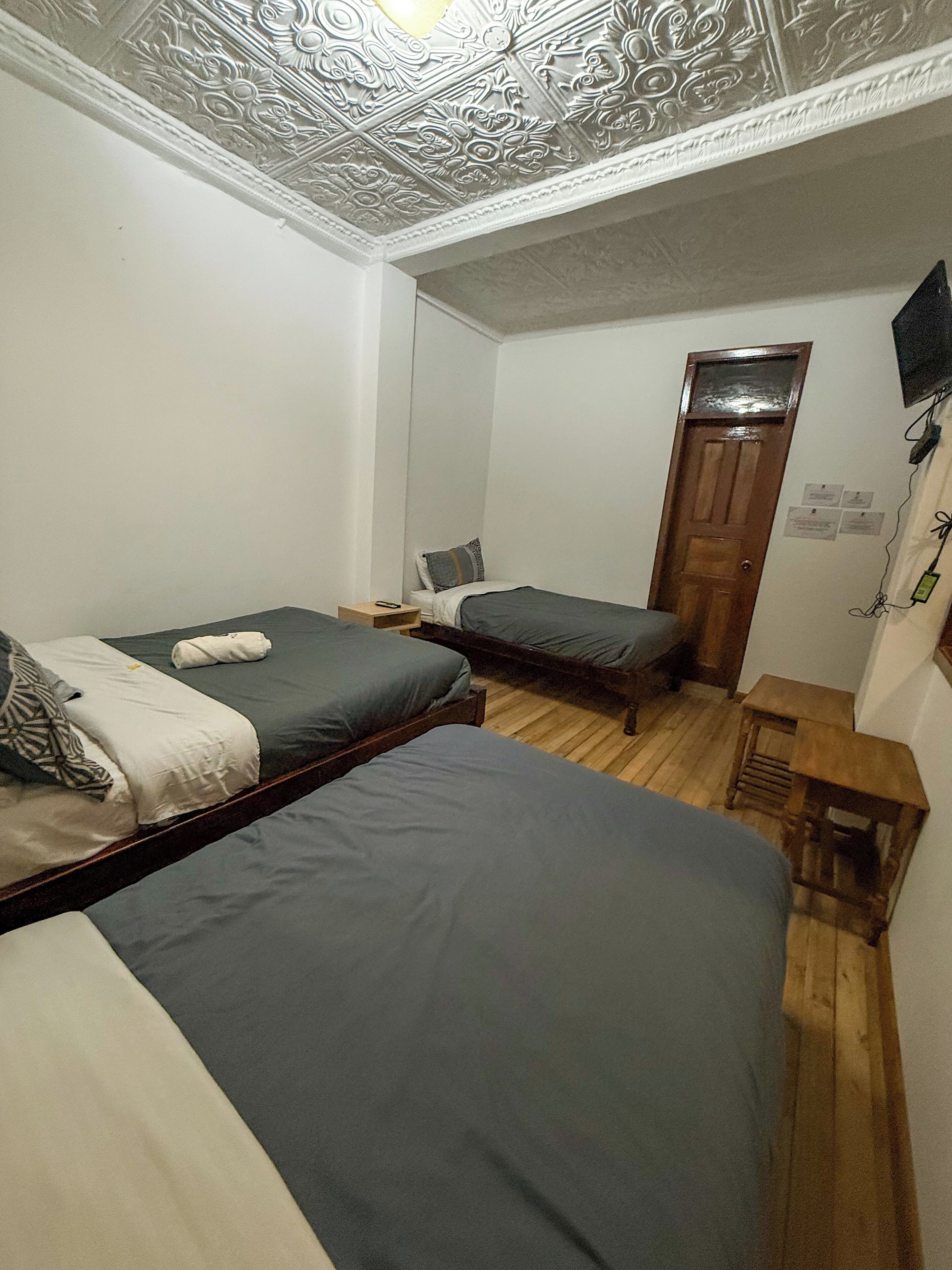 A room with two beds, a wooden floor, a wooden door, and a small table.