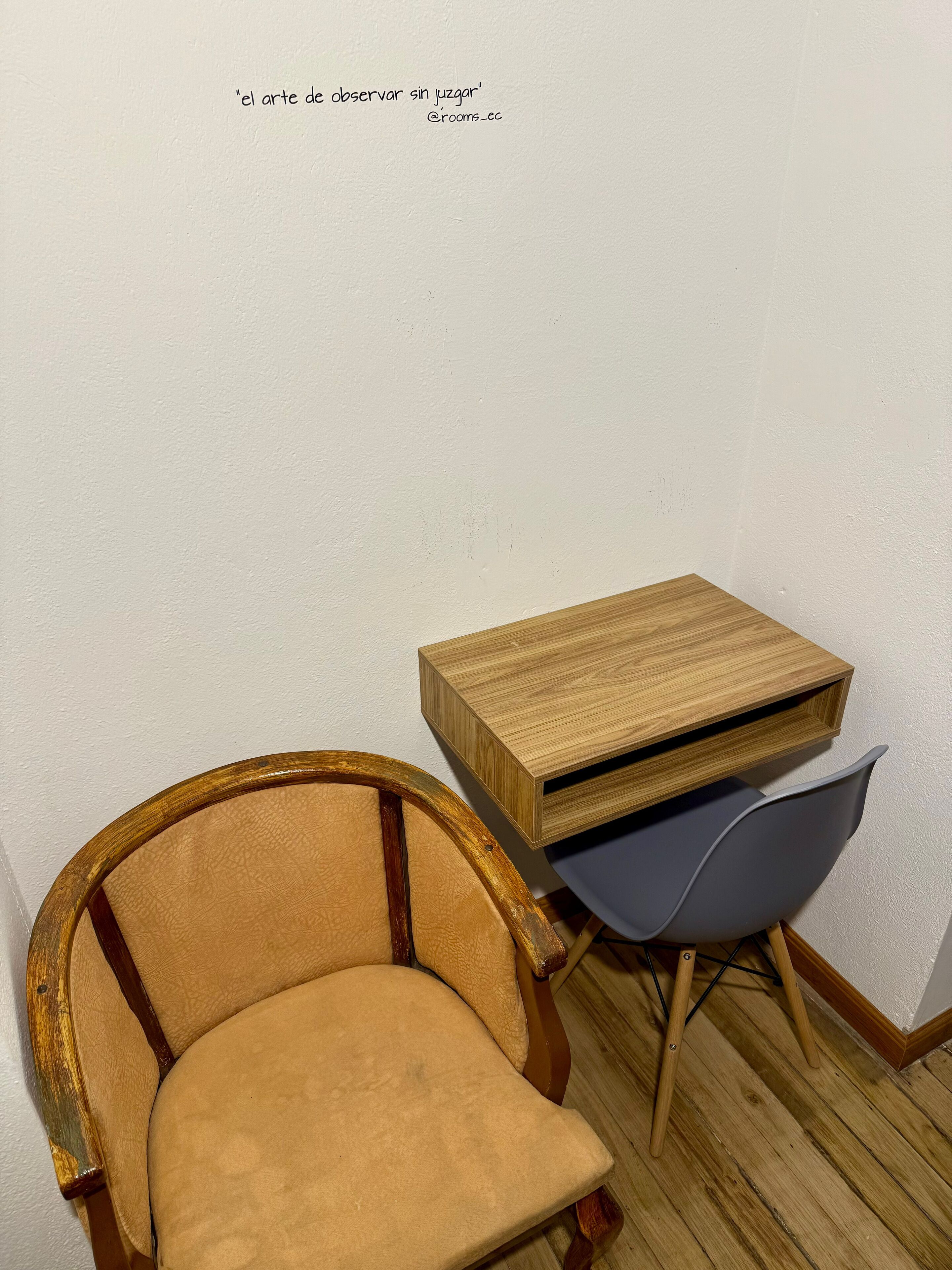 A corner of a room with a wooden chair, a small wooden table, and a blue chair.