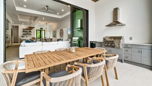 A modern kitchen with a built-in grill, a dining area with a wooden table and wicker chairs, and a living area with a sofa and a coffee table. - NEW! Luxury 6BR Villa w/ Pool & Spa (Naples)