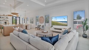 A modern living room with a large TV, comfortable seating, and a kitchen area. - NEW! Luxury 6BR Villa w/ Pool & Spa (Naples)