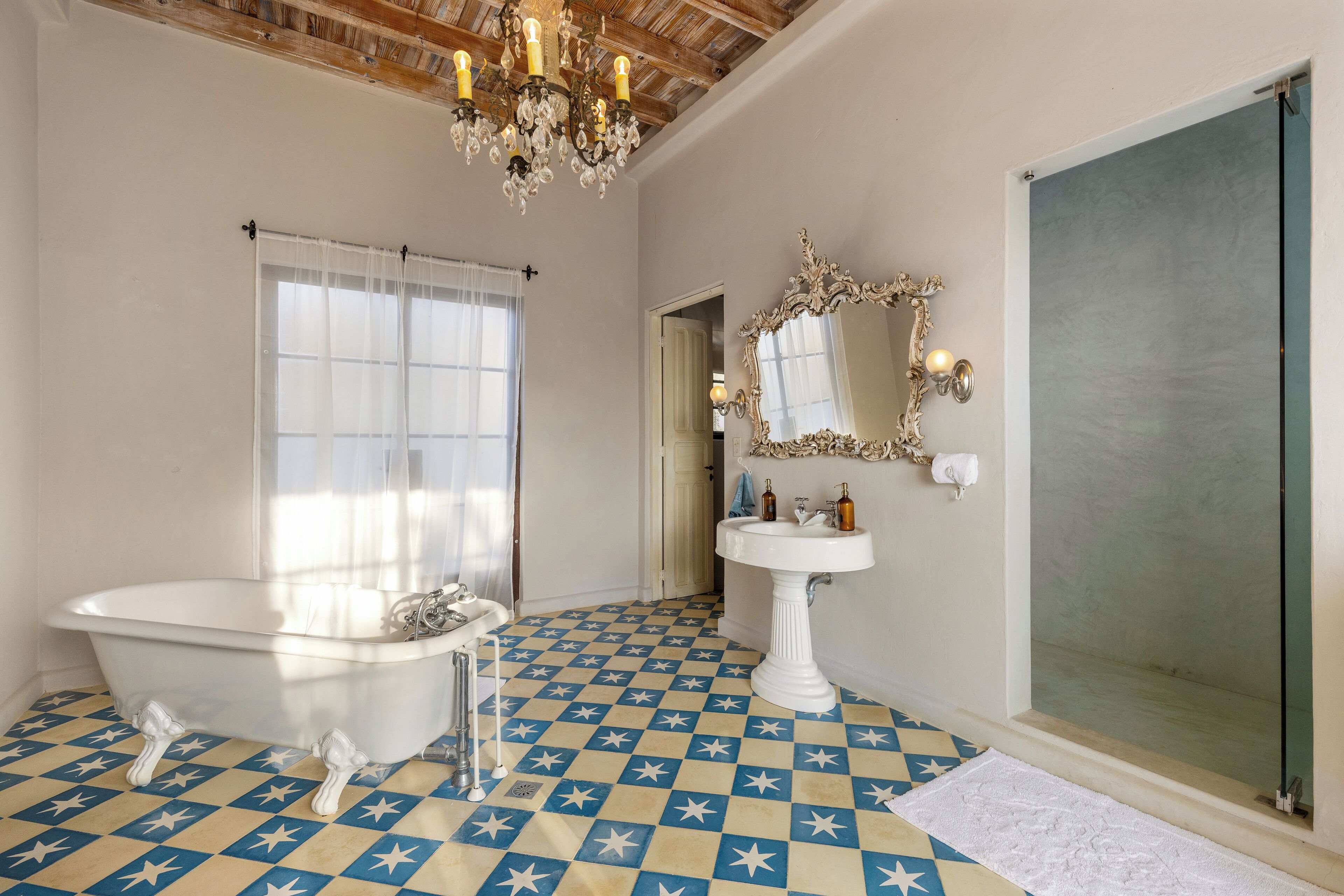 A bathroom with a star-patterned floor, a clawfoot bathtub, a pedestal sink, a large mirror, and a chandelier.