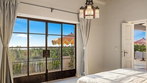 A bedroom with a large window, a bed, and a chandelier. - Grand Villa del Mar (Todos Santos)