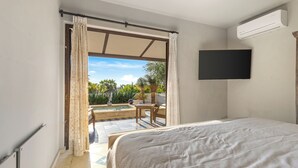 A bedroom with a bed, a television mounted on the wall, and an open sliding door leading to a patio with a pool and outdoor furniture. - Grand Villa del Mar (Todos Santos)