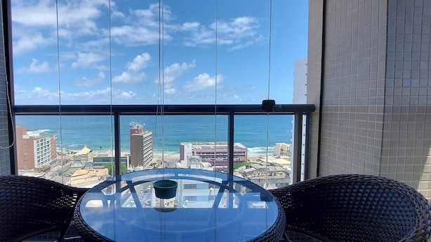 Un balcón con una mesa de vidrio y sillas de mimbre, con vistas a la ciudad y al océano.