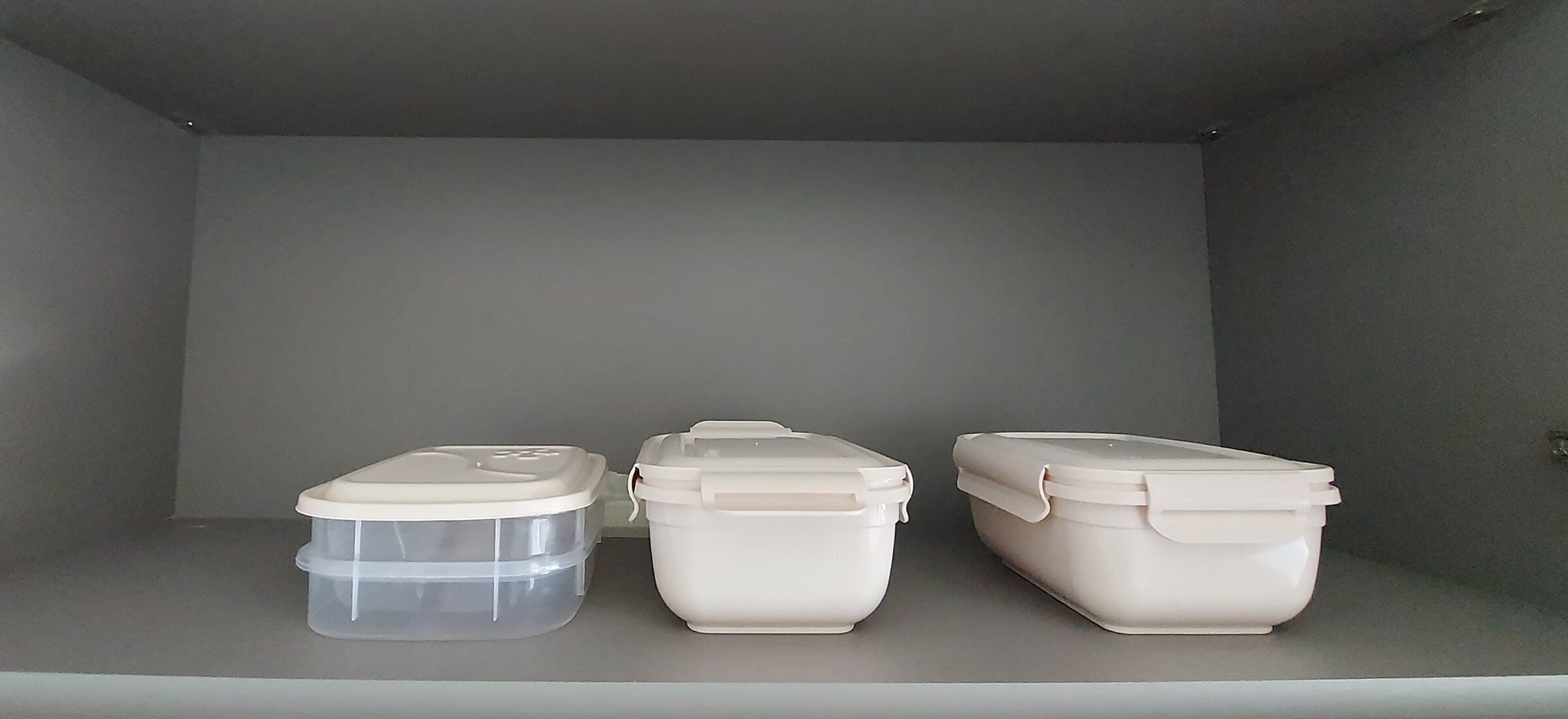 Three storage containers on a shelf in a room with plain walls and a neutral color scheme.
