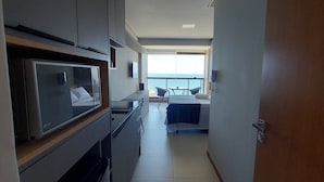 Habitación de hotel moderna con kitchenette, una cama, un balcón con vista al mar y un televisor montado en la pared.