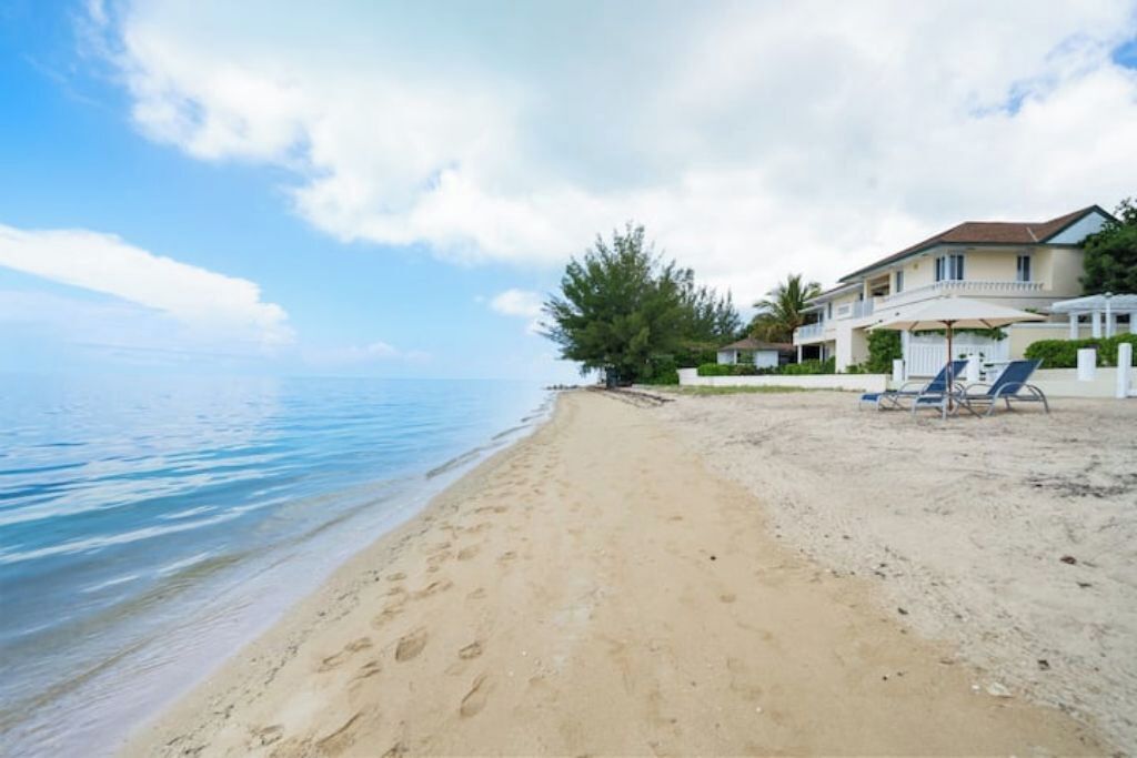A beach with a sandy shore, a few lounge chairs, and a building with a balcony.