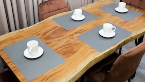Een houten vergadertafel met vier witte kopjes en schoteltjes, grijze placemats en bruine gestoffeerde stoelen.