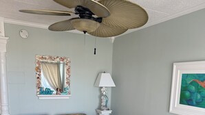 Una habitación con dos sofás de estampado floral, un ventilador de techo, un espejo con marco de concha marina, una lámpara y un cuadro enmarcado.