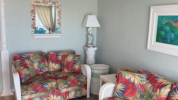 A room with two floral-patterned sofas, a ceiling fan, a mirror with a seashell frame, a lamp, and a framed painting.