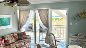 A room with a sofa, wicker chairs, a glass table, and a ceiling fan.