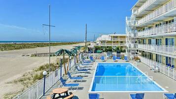 A hotel with a swimming pool, beach view, and multiple balconies.