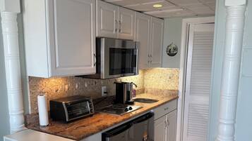 A compact kitchen with white cabinets, a stainless steel microwave, a toaster, and a sink.