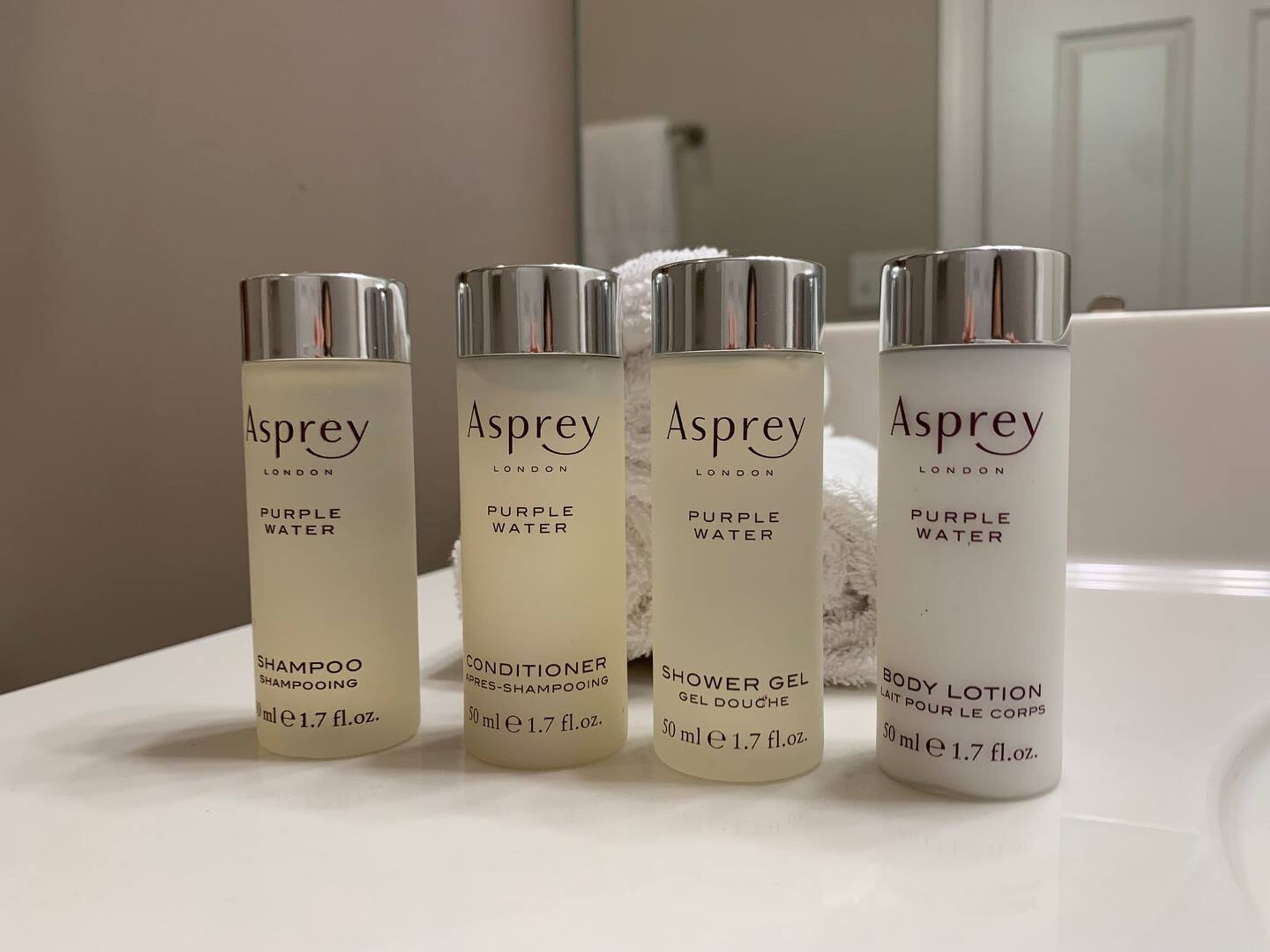 Quatre flacons de produits Asprey London sont posés sur le comptoir d’une salle de bain.