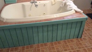 Een badkamer met een vrijstaand bad, betegelde vloer en een groene wand.