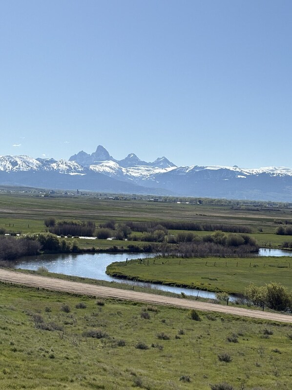 Un paysage rural avec une rivière, un chemin de terre et, au loin, des montagnes enneigées.