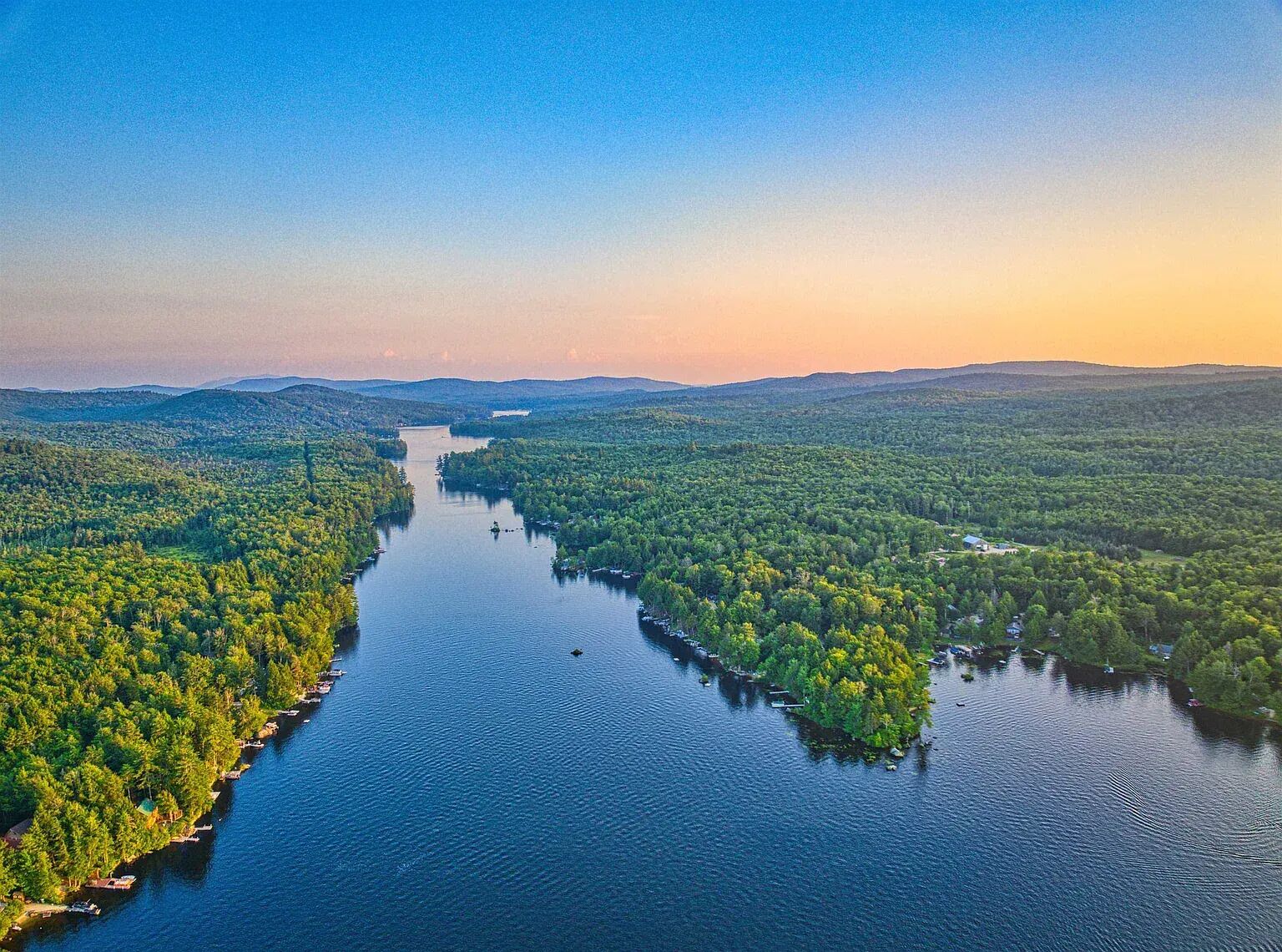 A river surrounded by dense forest with boats docked along the banks.