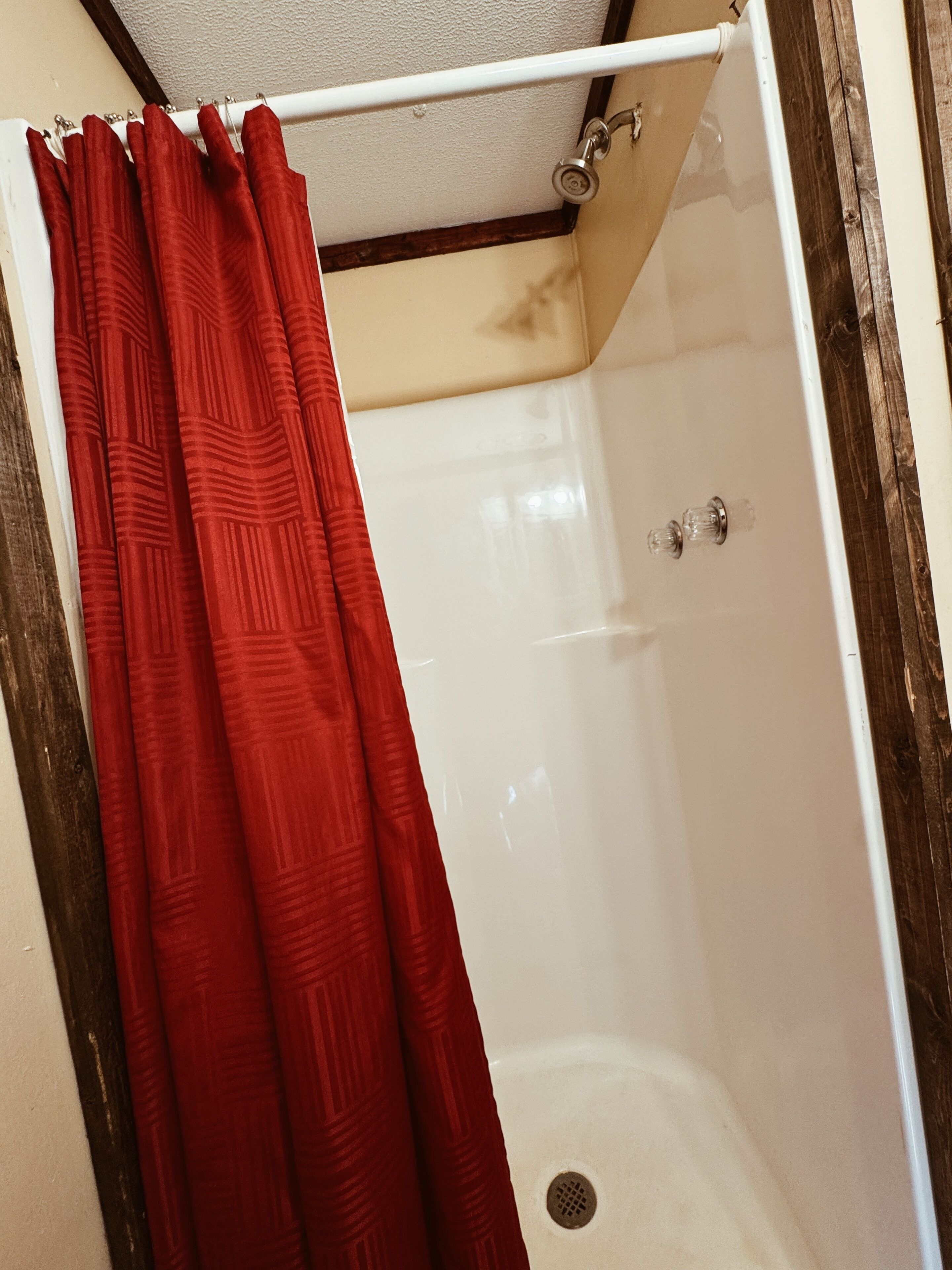 A shower with a red curtain, a white bathtub, and a wooden frame around the shower area.