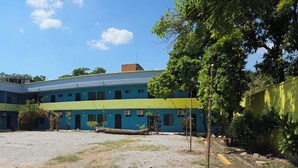 A multi-story building with a courtyard, featuring a mix of blue and green colors, surrounded by trees and a gravel ground. - Hotel Tamuín (Tamuín)
