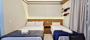 A hotel room with two single beds, a wooden headboard, a small desk, and a window with curtains.