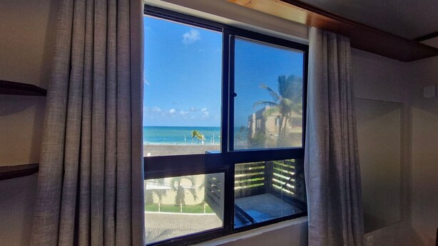 A room with a large window overlooking a beach and a wooden deck.