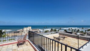 A rooftop terrace with a view of the ocean, featuring a bench and a chair.