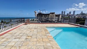 A rooftop swimming pool with a view of the ocean and a city skyline.