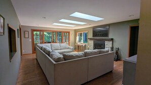 Uma sala de estar moderna com um amplo sofá modular, claraboias, lareira e janelas grandes.