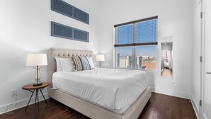 A bedroom with a large bed, two bedside lamps, a ceiling fan, and a window with blinds.