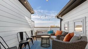 A covered outdoor seating area with wicker furniture, a blue rug, and string lights.