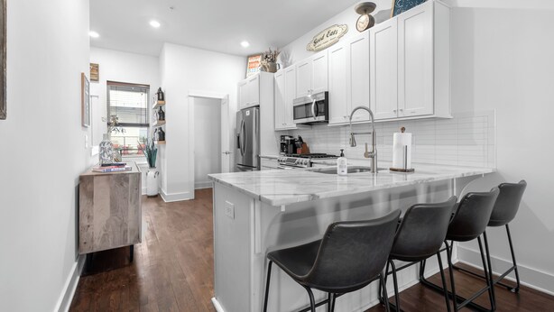 A modern kitchen with white cabinets, a central island with bar stools, a refrigerator, microwave, and a sink.