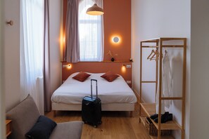 Quarto de hotel bem arrumado, com uma cama, área de estar, armário e mala.