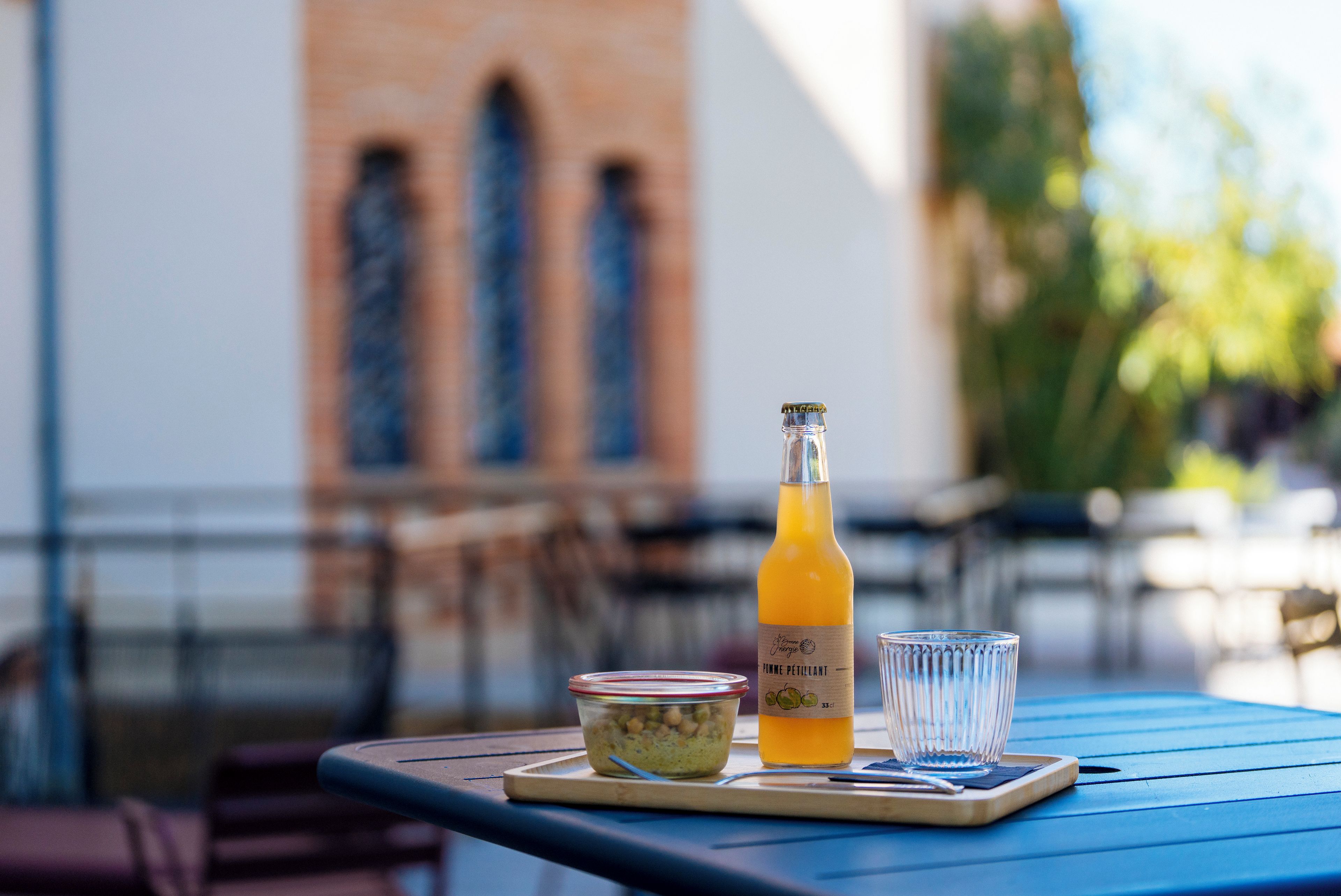 A table with a bottle of orange juice, a glass, and a container of food on a blue table.
