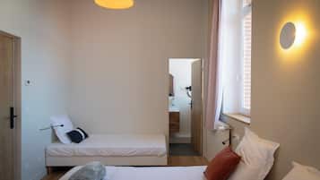 Un dormitorio pequeño y bien iluminado con dos camas, una ventana con persianas, una puerta y una lámpara.