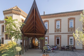 A courtyard with a wooden pavilion, outdoor seating, and a building with arched windows. - Hotellerie De L'abbaye Du Désert (Thil)