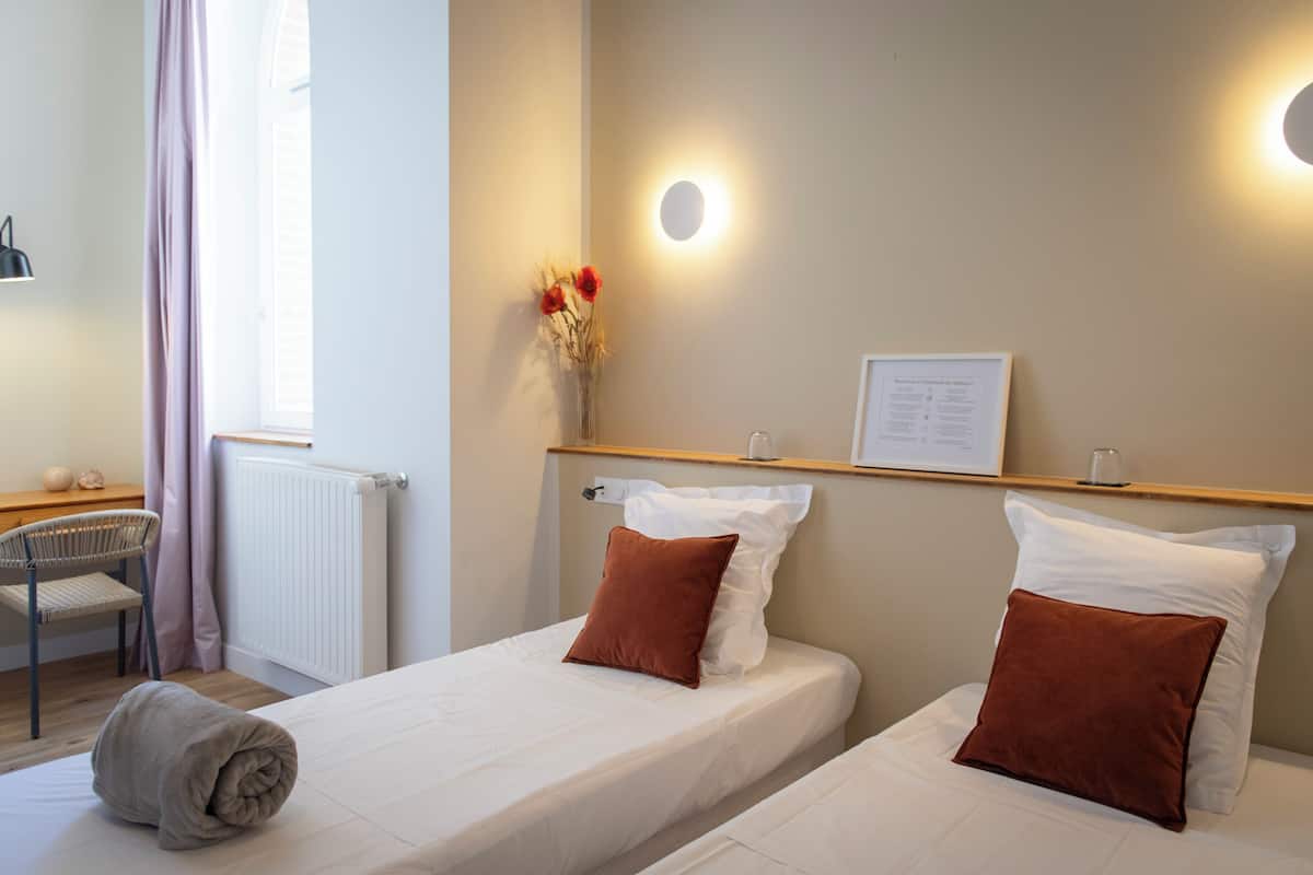 Een hotelkamer met twee bedden, een bureau, een stoel, een radiator, een wandlamp en een lijst aan de muur.