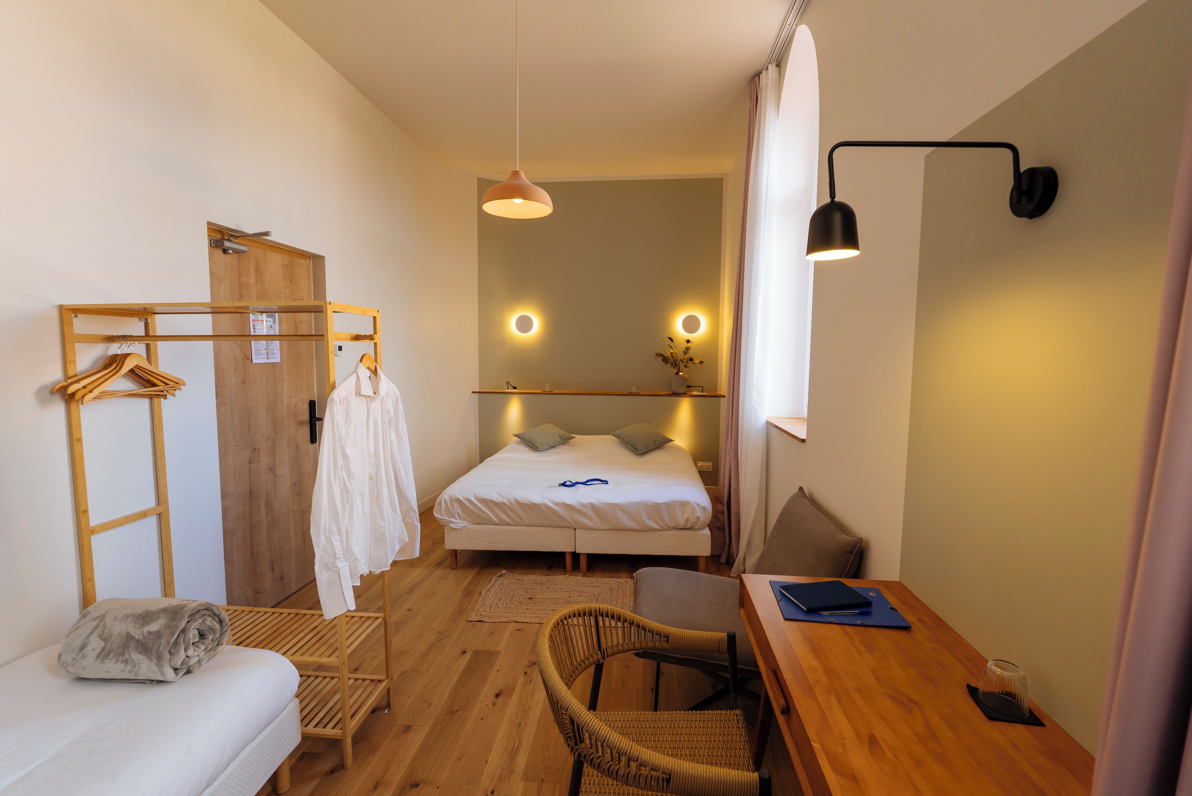 Una habitación de hotel compacta con cama, escritorio, silla, armario y espejo.