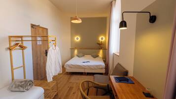 Una habitación de hotel compacta con cama, escritorio, silla, armario y espejo.
