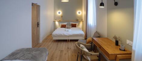 A modern bedroom with a wooden floor, a bed with white bedding, a small desk with a chair, and a pendant light above the bed.