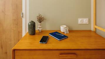 A wooden desk with a lamp, a vase, a mug, a notebook, and a smartphone.