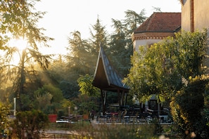 A pavilion with a sloped roof surrounded by trees and a building with a tiled roof. - Hotellerie De L'abbaye Du Désert (Thil)
