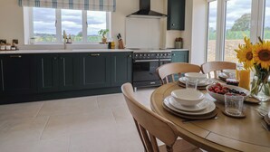 A modern kitchen with dark green cabinets, a black stove, and a window with a view of the outdoors. - The Fox Den (Yeovil)