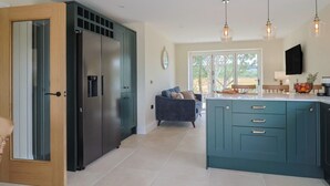 A modern kitchen with teal cabinets, a central island, and pendant lighting. - The Fox Den (Yeovil)
