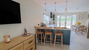 A modern kitchen with a bar area, wooden chairs, and a flat-screen TV mounted on the wall. - The Fox Den (Yeovil)