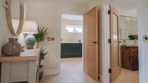 A hallway leading to a kitchen with a wooden door, a mirror, a vase, and a lamp. - The Fox Den (Yeovil)