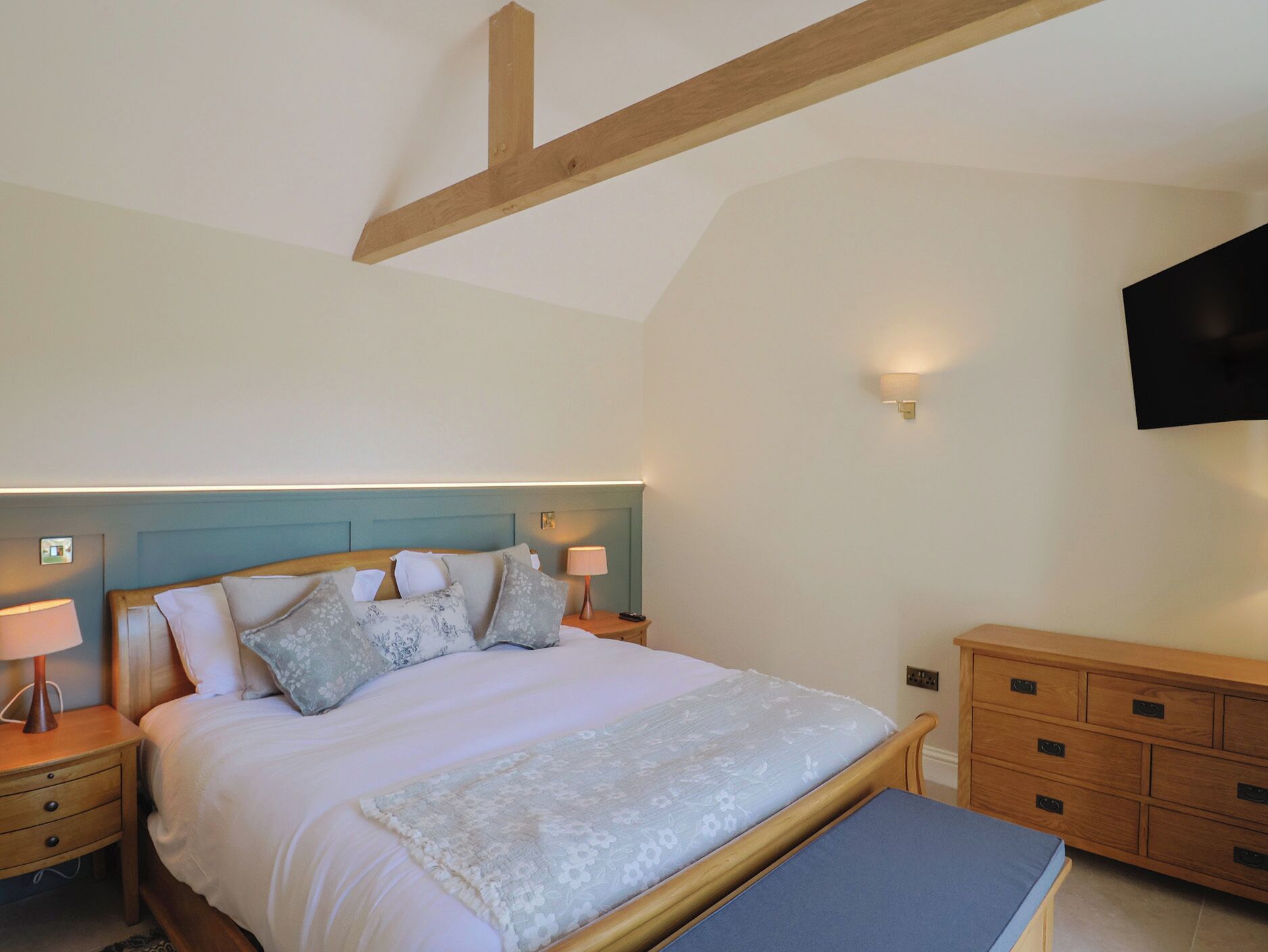 A bedroom with a bed, bedside tables, a nightstand, a dresser, and a mounted TV.