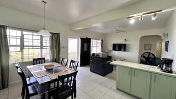 A spacious living area with a dining table, chairs, a sofa, a kitchen island, and a TV mounted on the wall.